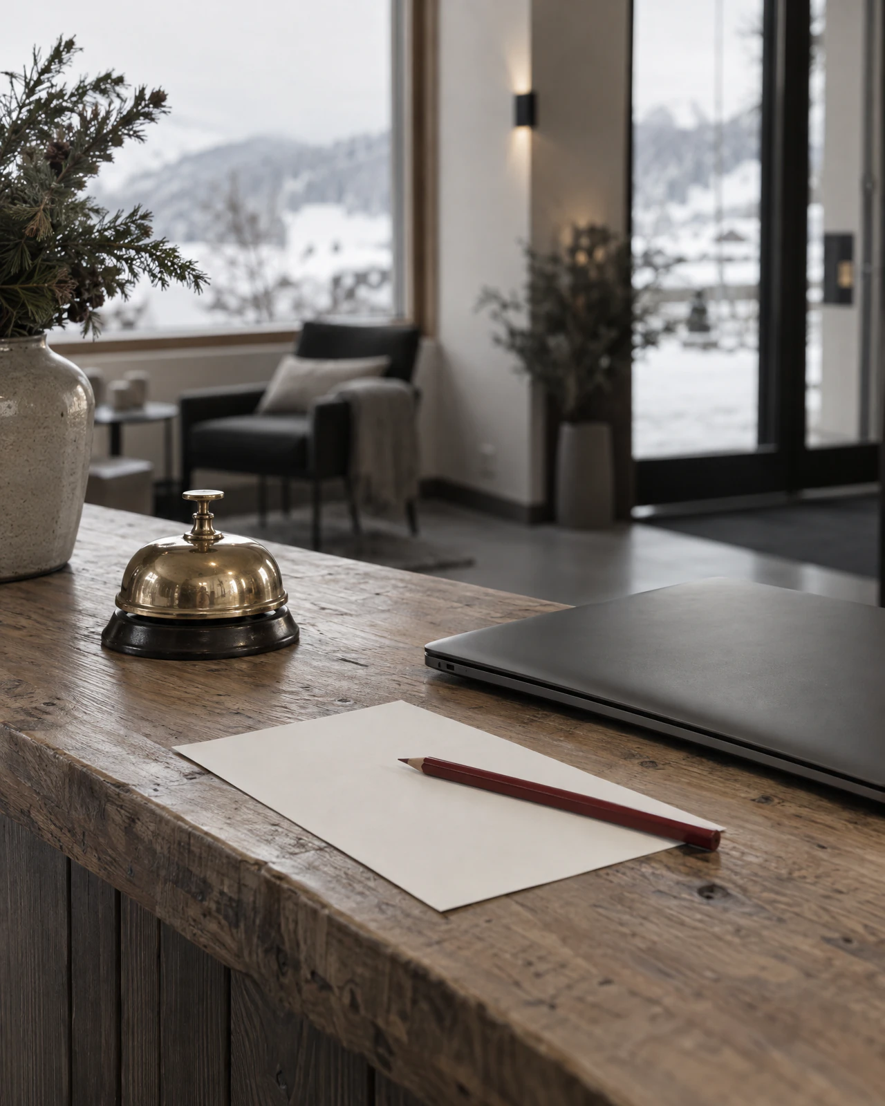 Messingglocke, Notizpapier mit Bleistift und geschlossener Laptop auf einem Holztresen, draussen Schnee